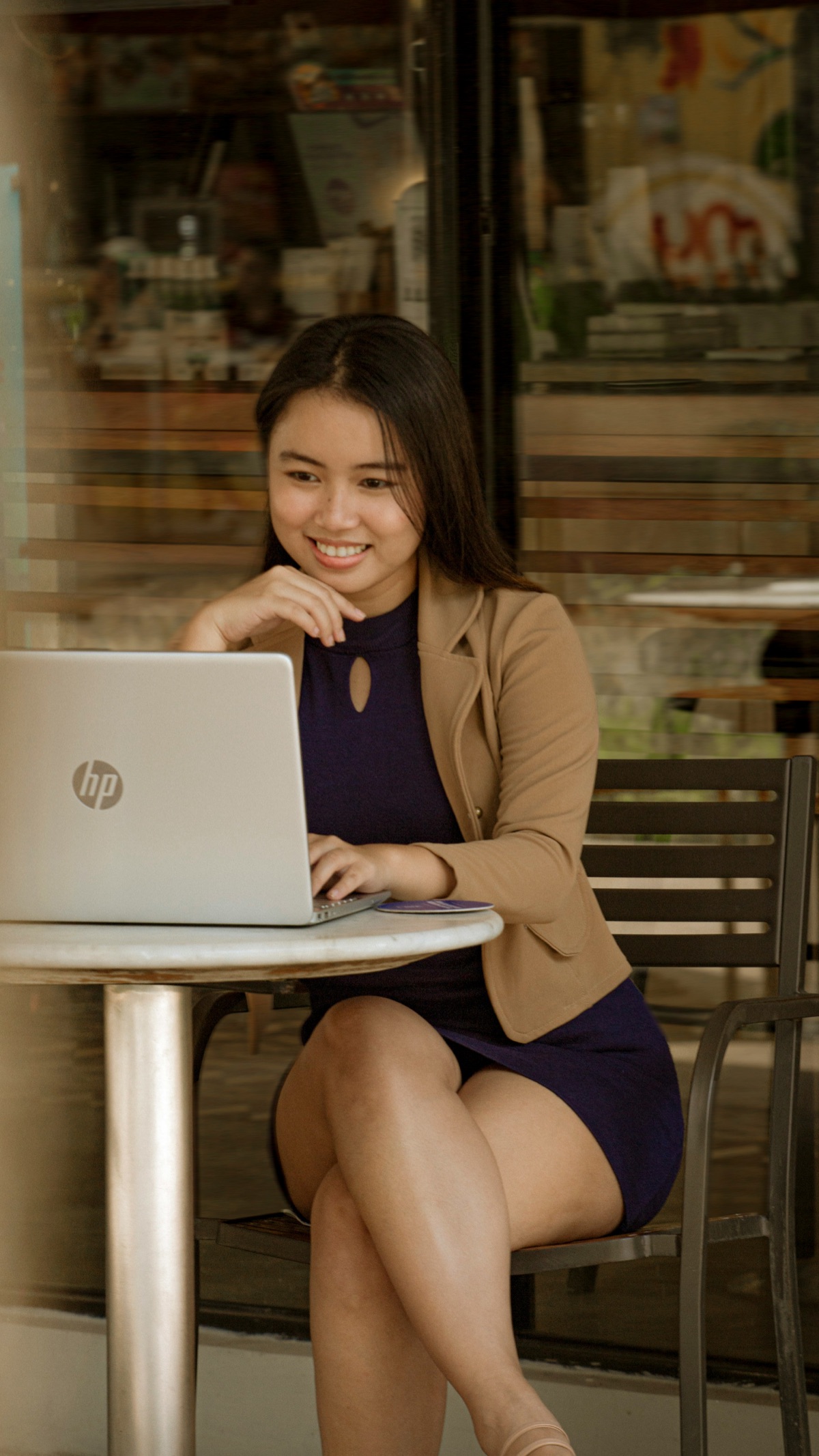 Professional woman in a blazer working on a laptop at an outdoor cafe table, focused on her screen